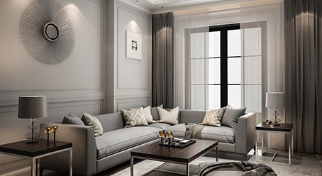 A modern living room in a Nyati Emerald 2 & 3 BHK flat in Baner features a gray sectional sofa with decorative cushions, two side tables with lamps, a large window with sheer curtains, and contemporary wall art.