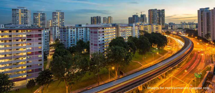 A vibrant urban neighborhood with modern residential buildings and a busy highway during dusk, showcasing well-lit streets and surrounding greenery.​